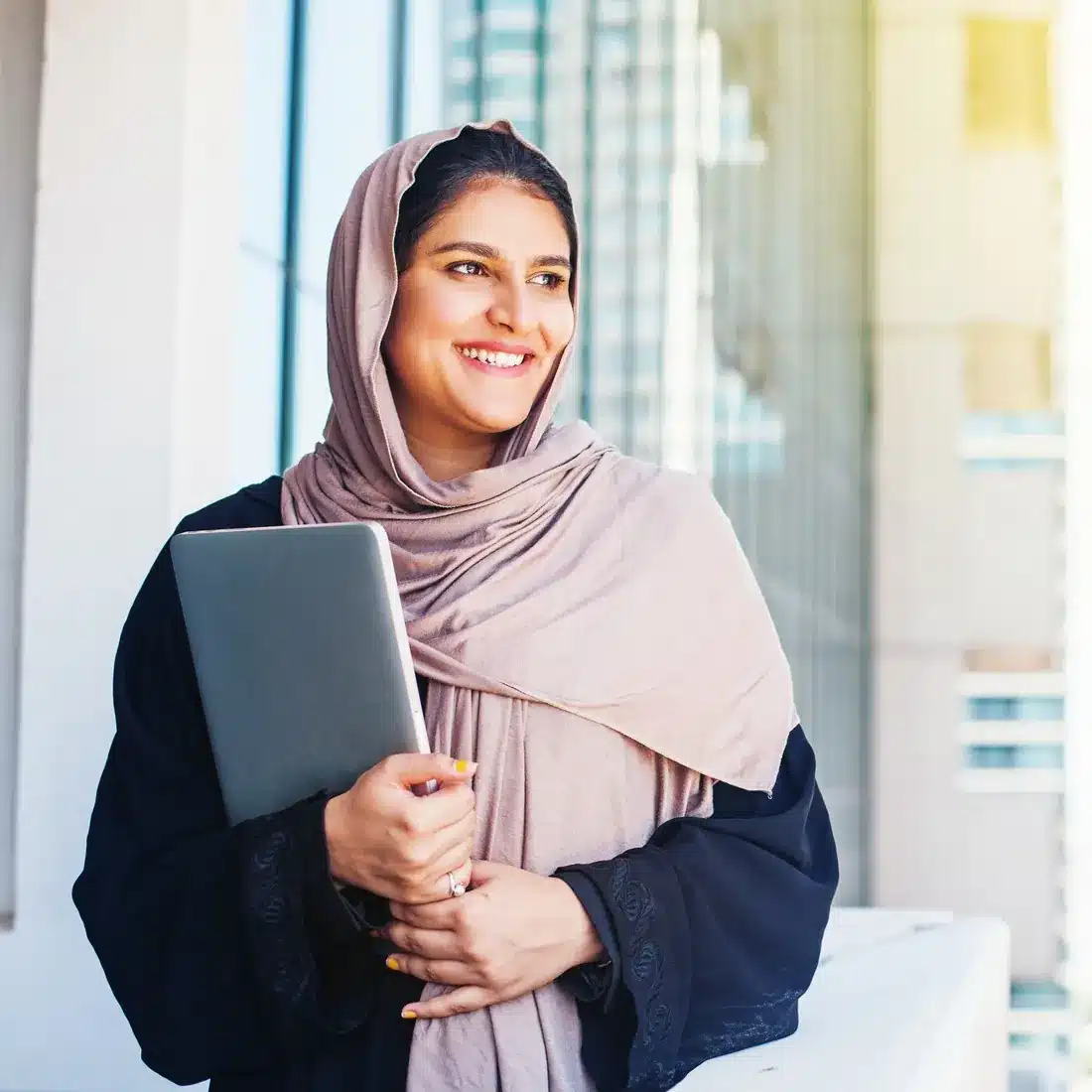 Smiling advisor in a hijab holding a tablet in a bright office