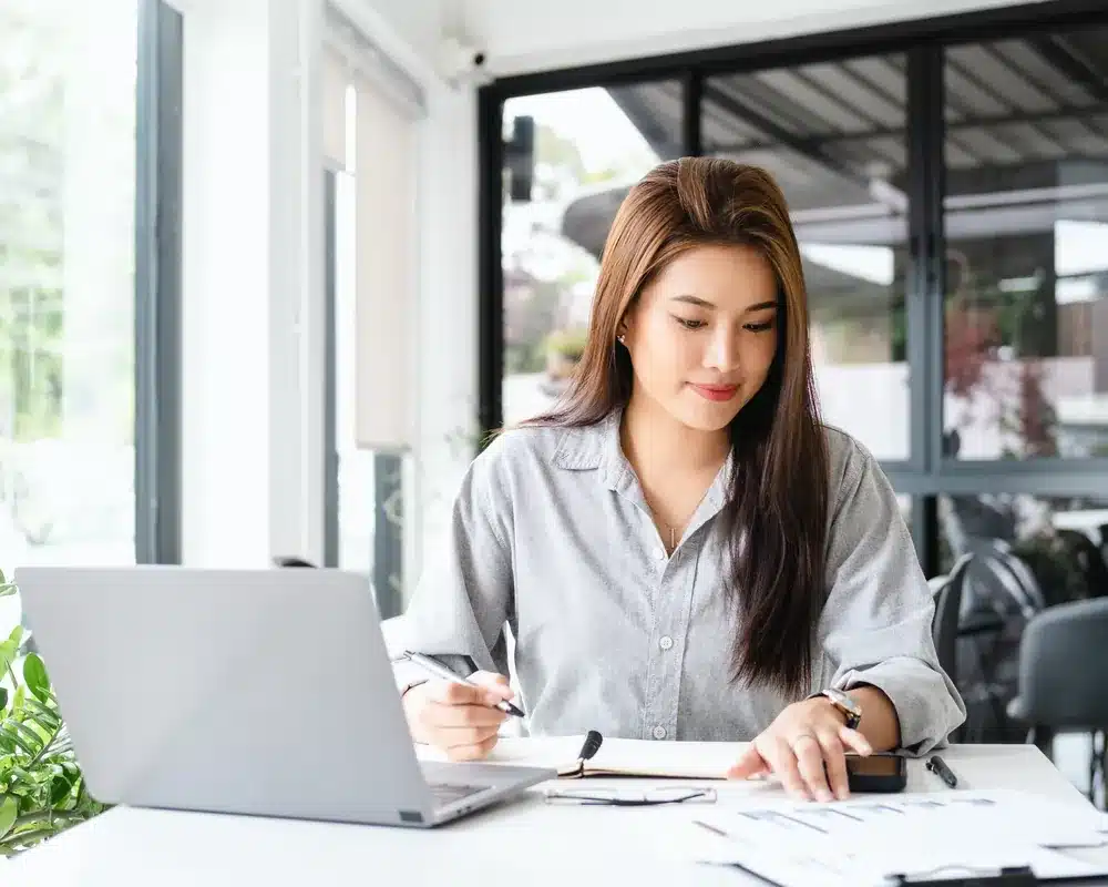 Business owner taking notes beside a laptop while reviewing how AI tools describe her company