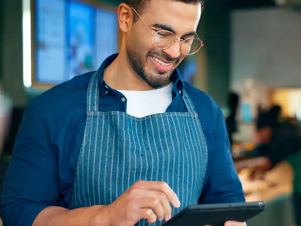 Cafe owner checking a tablet in his shop, managing email marketing for regular customers
