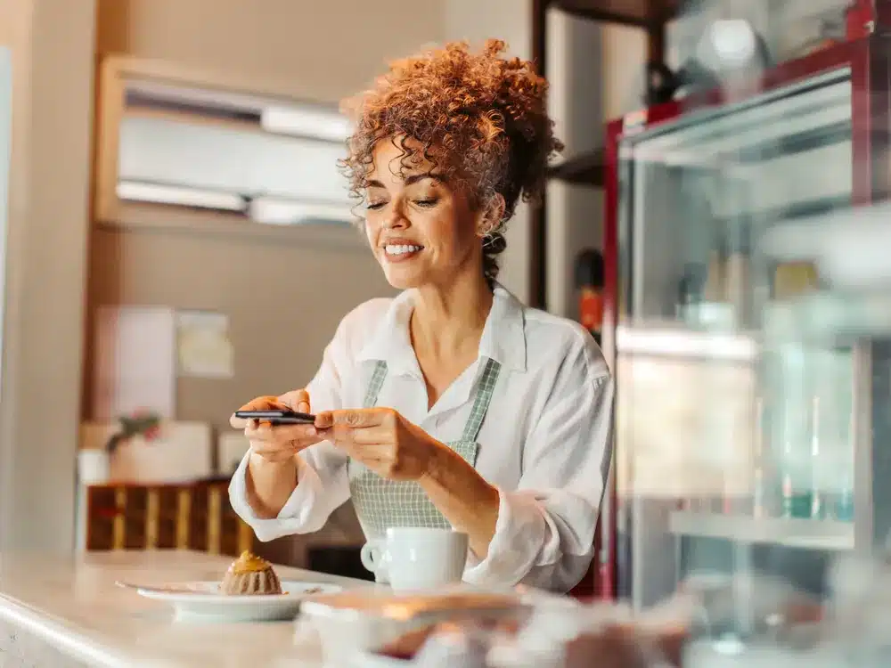Cafe owner photographing a pastry on the counter for social media content