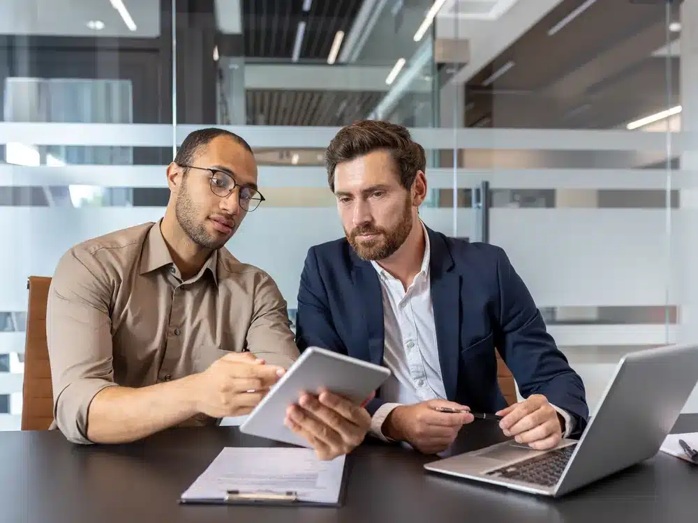 Two businessmen reviewing strategy on a tablet with a Fractional CMO in a modern office