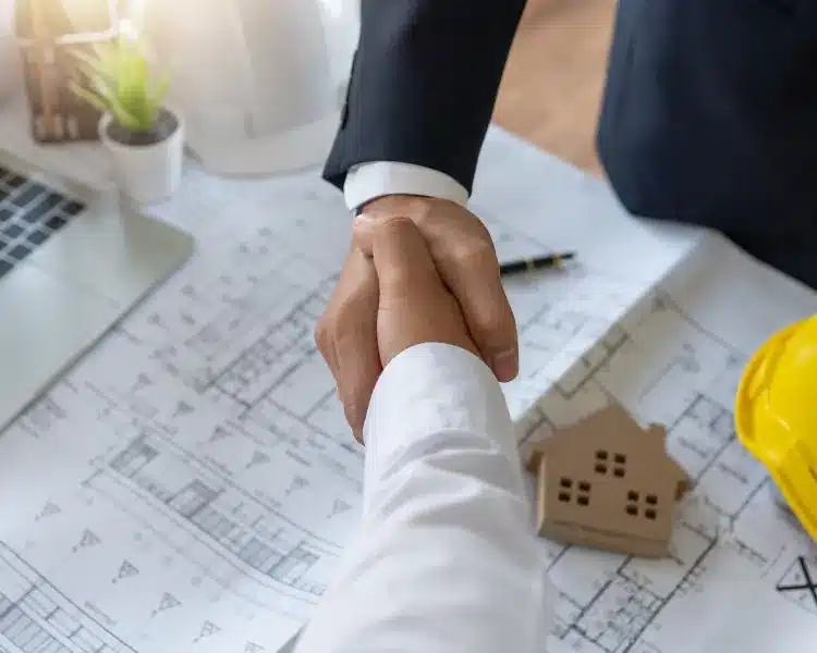Handshake over house plans and a model home
