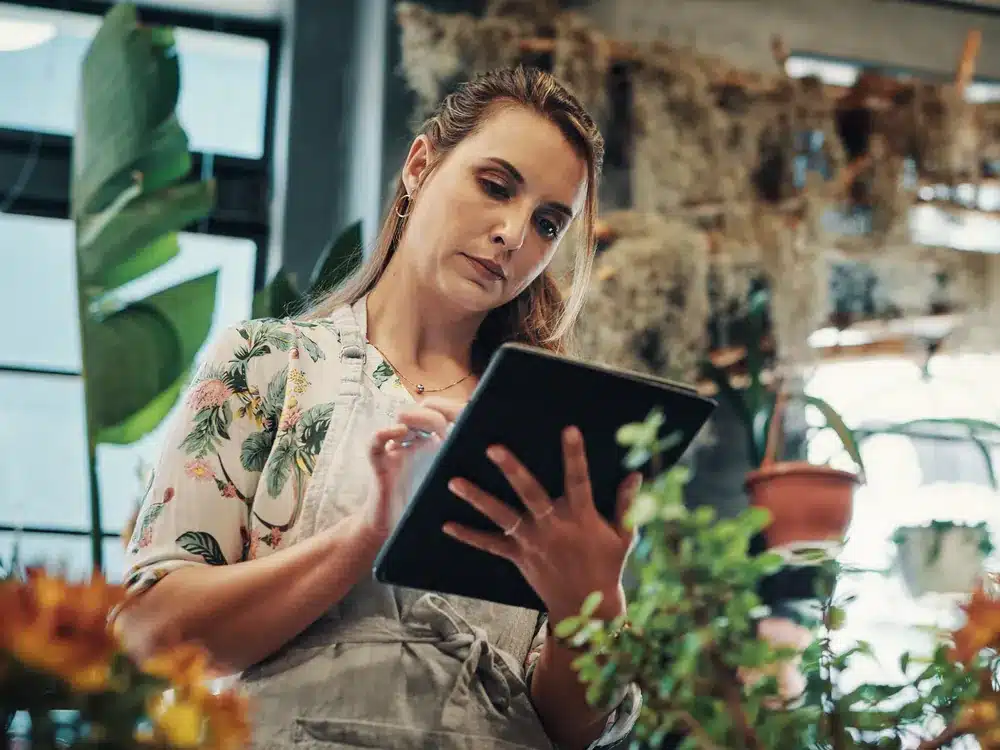 Plant shop owner using a tablet among greenery, planning a website design for her boutique