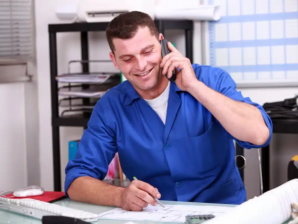 Search Visibility | CICOR Marketing Smiling tradesman on the phone at an office desk with blueprints, a typical local search visibility client